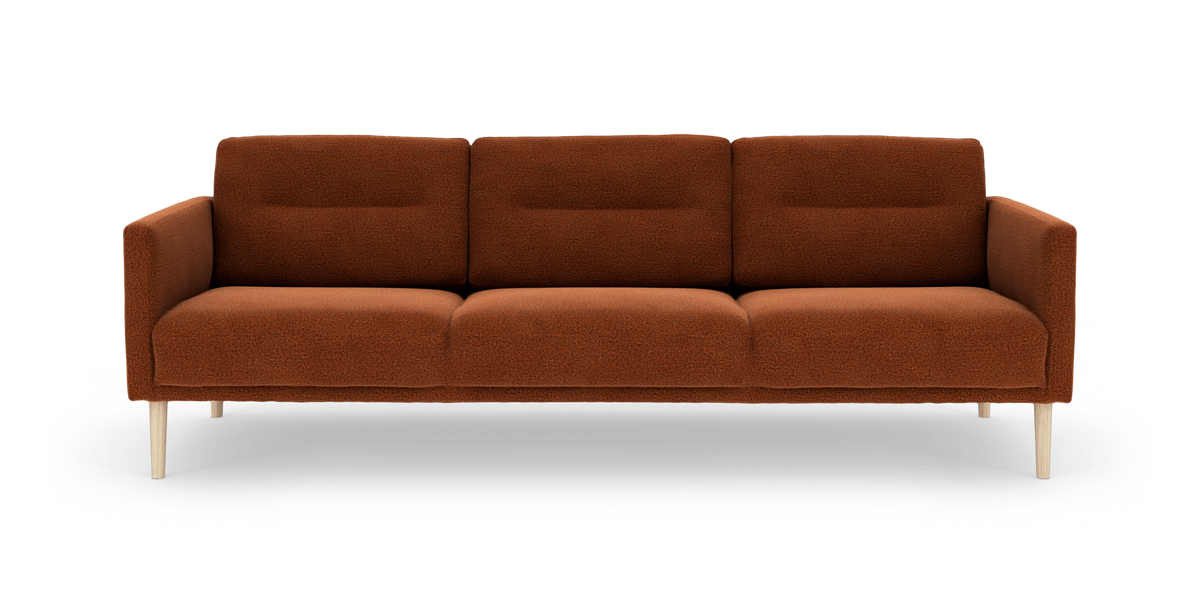 Tresædet rustbrunt stofsofa med lyse træben, set forfra på frilagt baggrund.