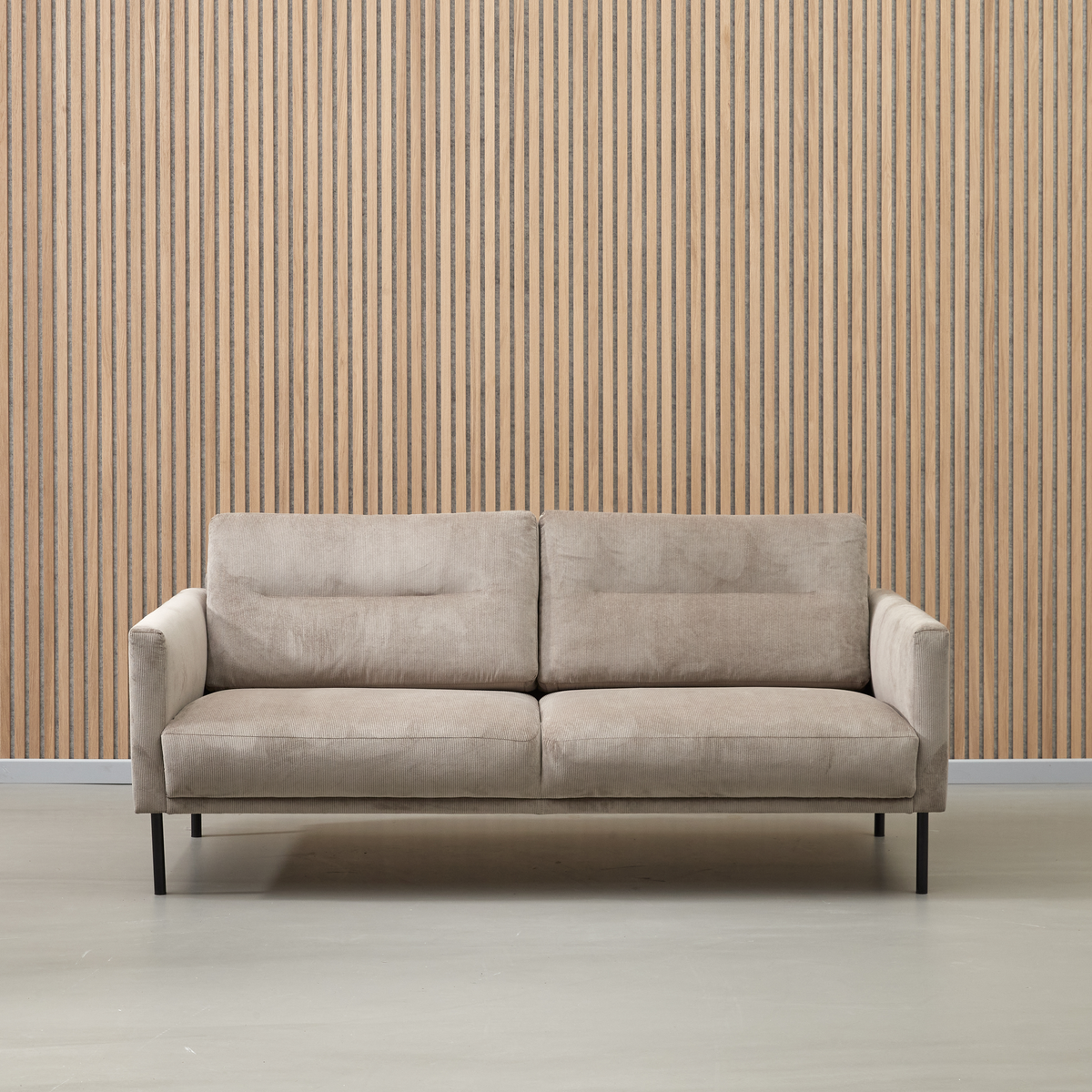Beige stofsofa med sorte ben foran en væg med lodrette trælameller.