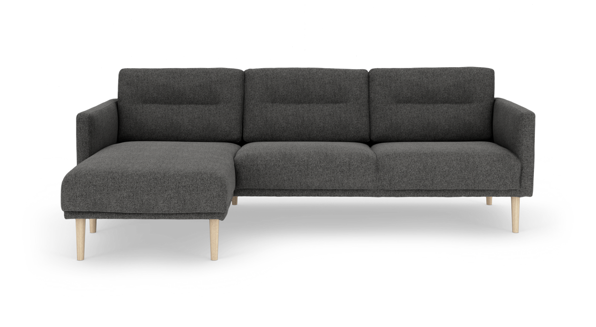 Mørkegrå hjørnesofa med chaiselong til venstre og lyse træben, frilagt på hvid baggrund.