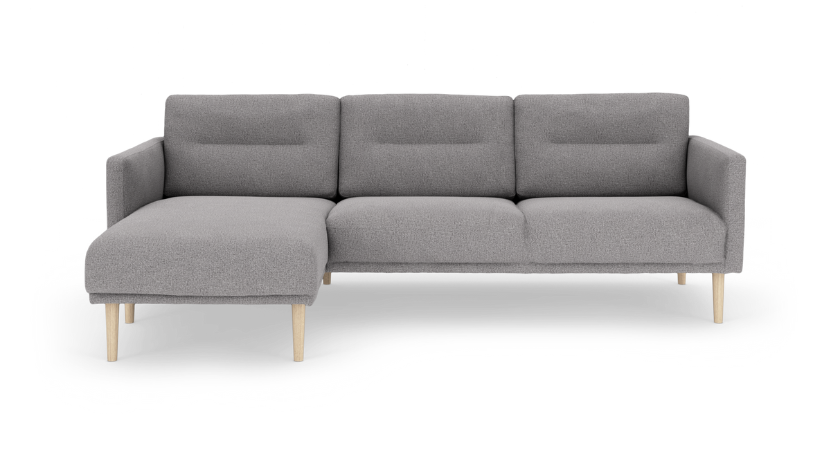 Grå modulsofa med venstrevendt chaiselong og lyse træben i frontvisning, frilagt mod hvid baggrund.