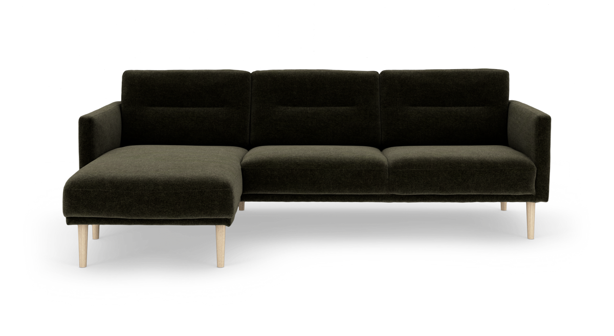 Mørkegrøn modulsofa med venstrevendt chaiselong og lyse træben, frilagt på hvid baggrund.