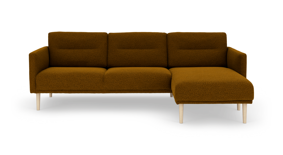 Hjørnesofa med chaiselong til højre i sennepsgul bouclé med lyse træben, fritlagt på hvid baggrund.