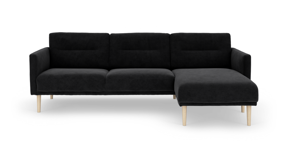 Sort hjørnesofa med chaiselong til højre og lyse træben, frilagt på hvid baggrund.