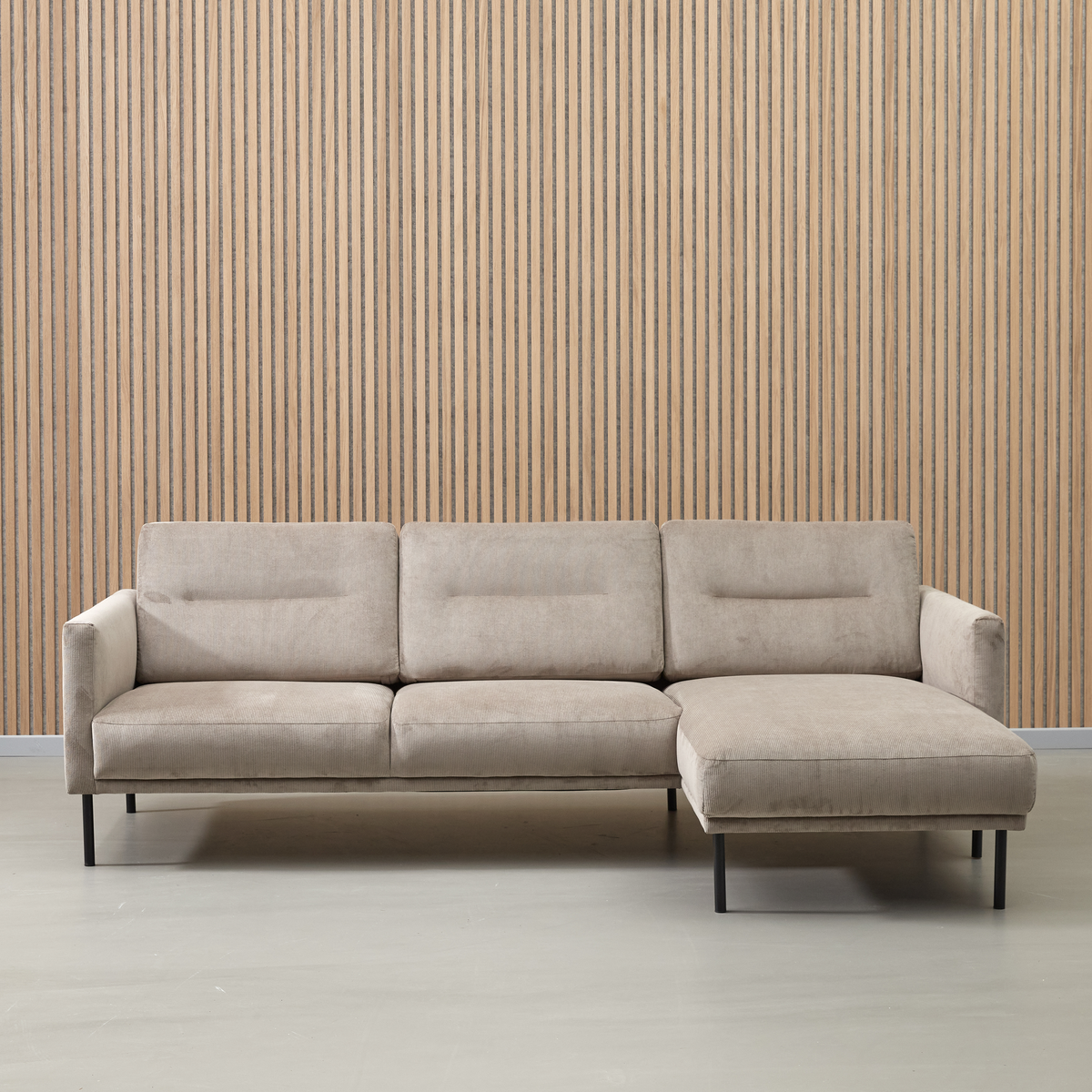 Beige hjørnesofa med chaiselong til højre foran en væg med lodrette træpaneler.