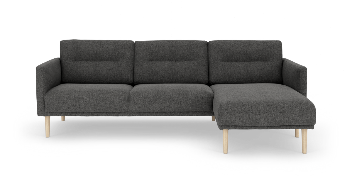Mørkegrå hjørnesofa med chaiselong til højre og lyse træben, frilagt på hvid baggrund.
