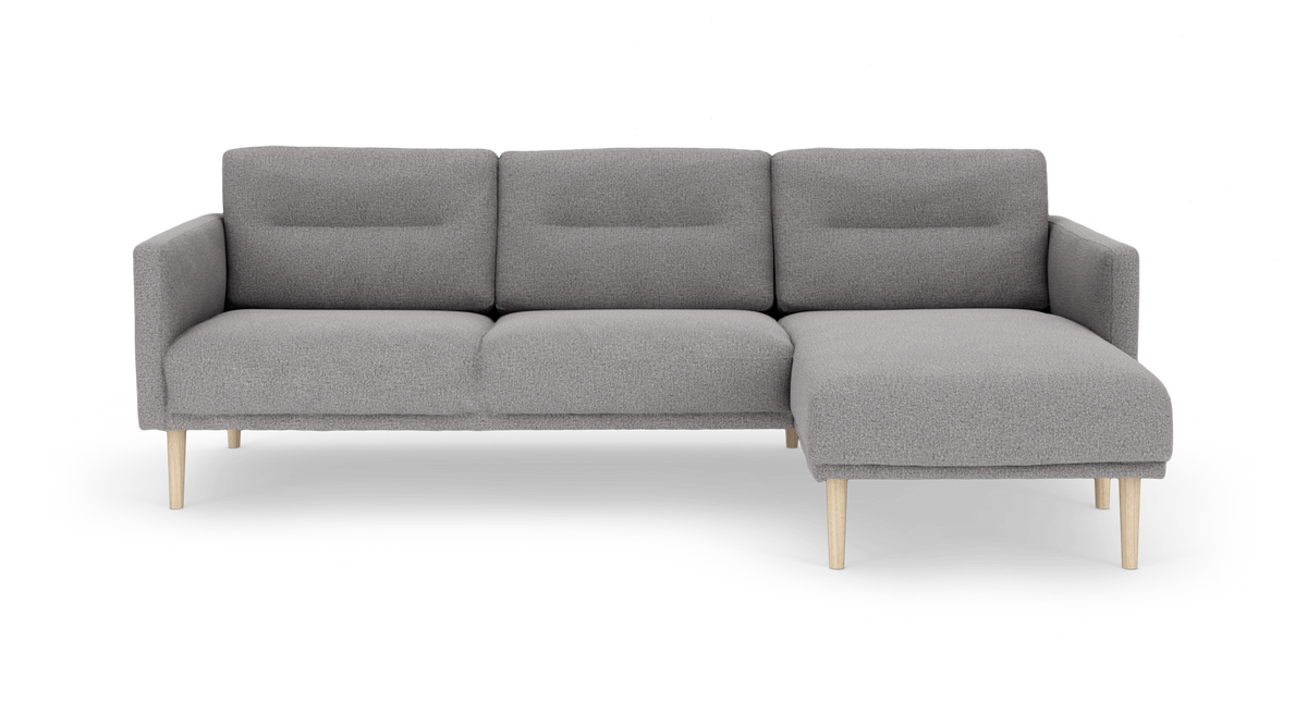 Grå tresæders sofa med højre chaiselong og lyse træben, frilagt på hvid baggrund.