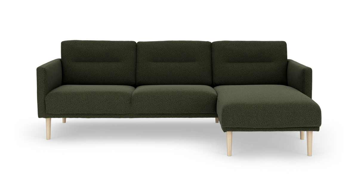 Mørkegrøn hjørnesofa med chaiselong til højre og lyse træben, frilagt på hvid baggrund.