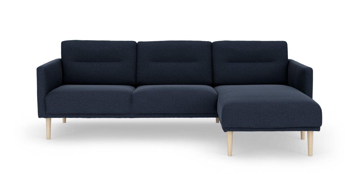 Mørkeblå 3-personers hjørnesofa med chaiselong til højre og lyse træben, frilagt på hvid baggrund.