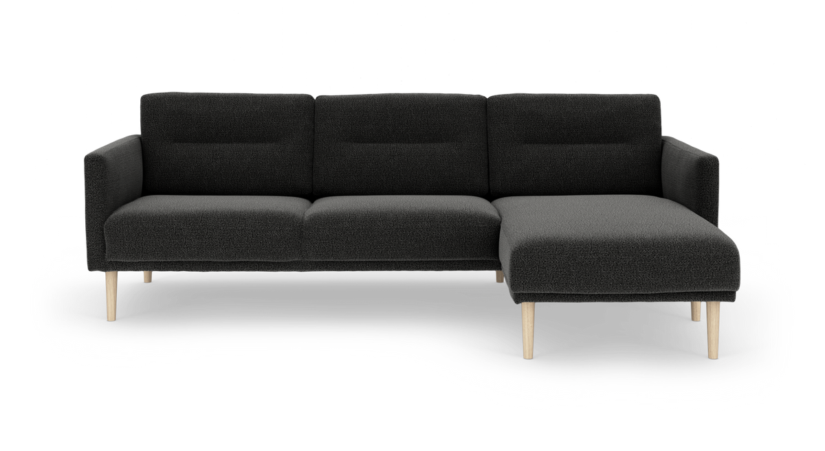 Mørkegrå sofa med chaiselong til højre og lyse træben, frontvisning på frilagt baggrund.