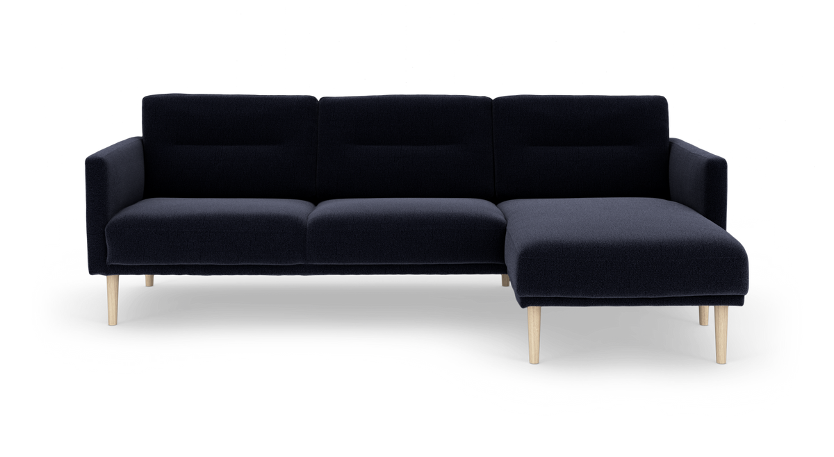 Mørkeblå hjørnesofa med chaiselong til højre og lyse træben, frilagt på hvid baggrund.