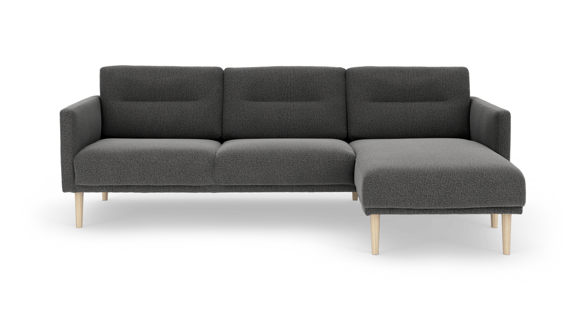 Mørkegrå modulsofa med chaiselong til højre og lyse træben, frontvisning i studiemiljø.