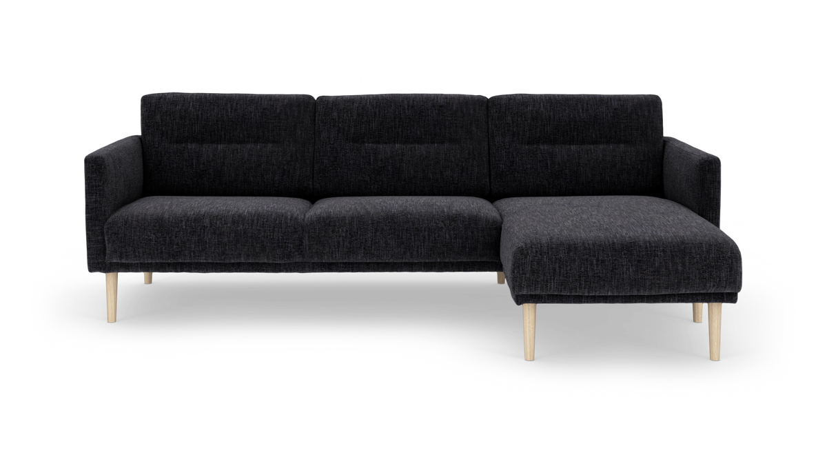 Mørkegrå modulsofa med chaiselong til højre og lyse træben, frilagt på hvid baggrund.