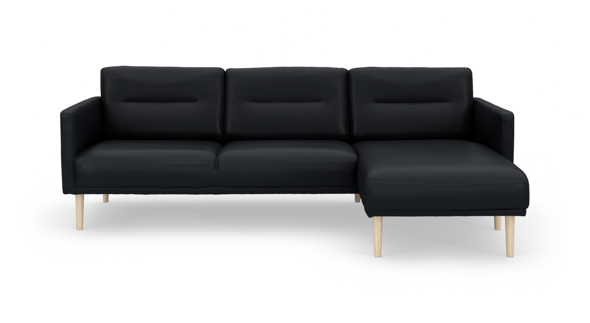 Sort hjørnesofa med chaiselong til højre og lyse træben, frilagt på hvid baggrund.