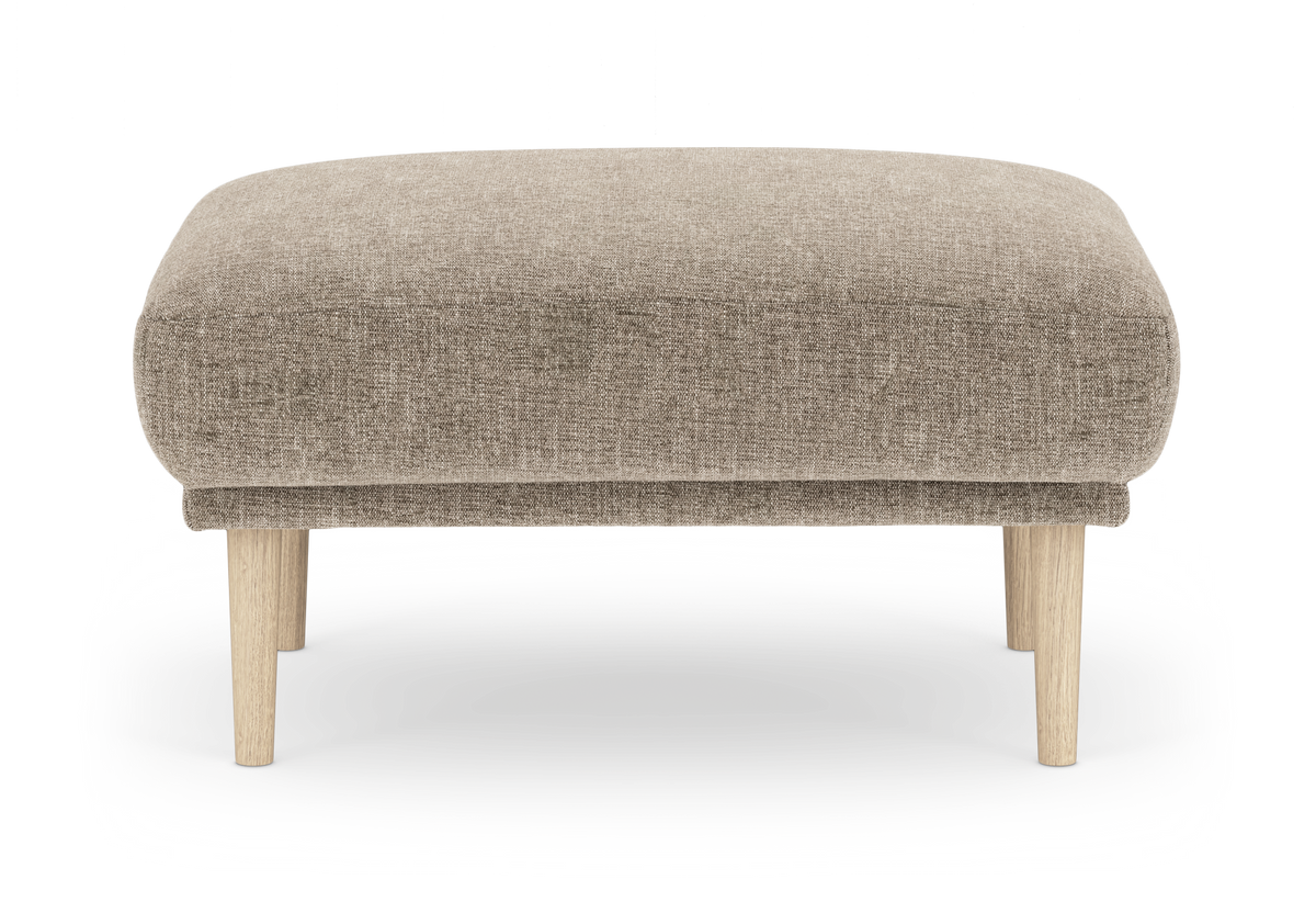 Beige fodskammel i stof med blødt afrundede kanter og lyse træben, frilagt på hvid baggrund.