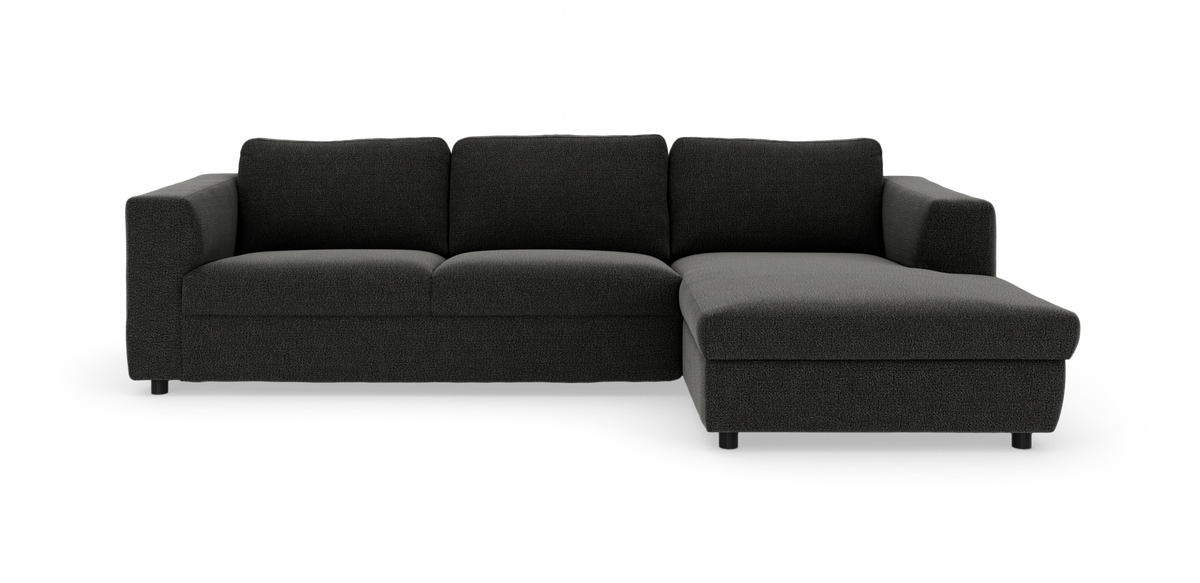 Mørkegrå hjørnesofa med chaiselong til højre, lav og lige profil i stof mod hvid baggrund.