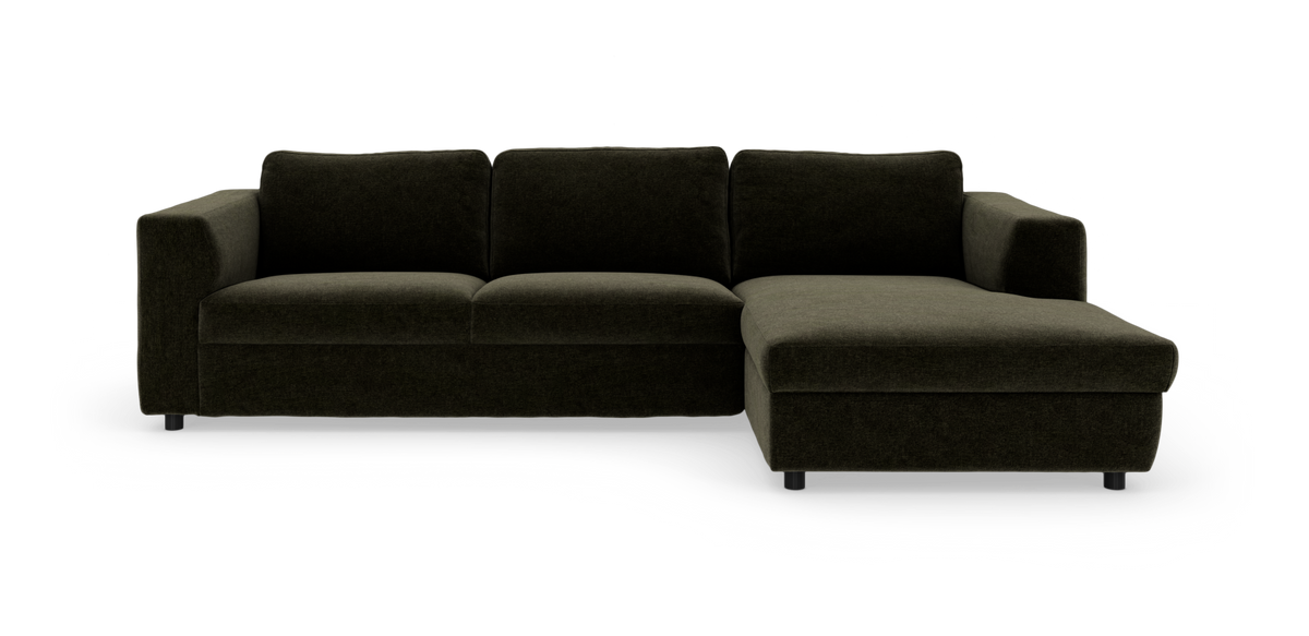 Mørkegrøn L‑sofa med højrevendt chaiselong, firesæder med fyldige puder på hvid frilægning.