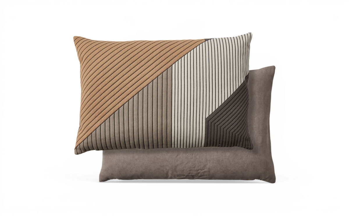 To pyntepuder, den øverste med ribbet geometrisk stribemønster i beige, grå og sort ovenpå en ensfarvet taupe-pude.