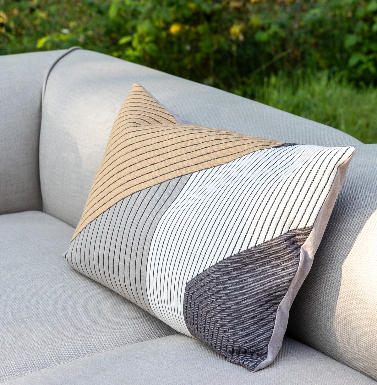 Stribet pyntepude i beige, hvid og grå på en lysegrå udendørs sofa.
