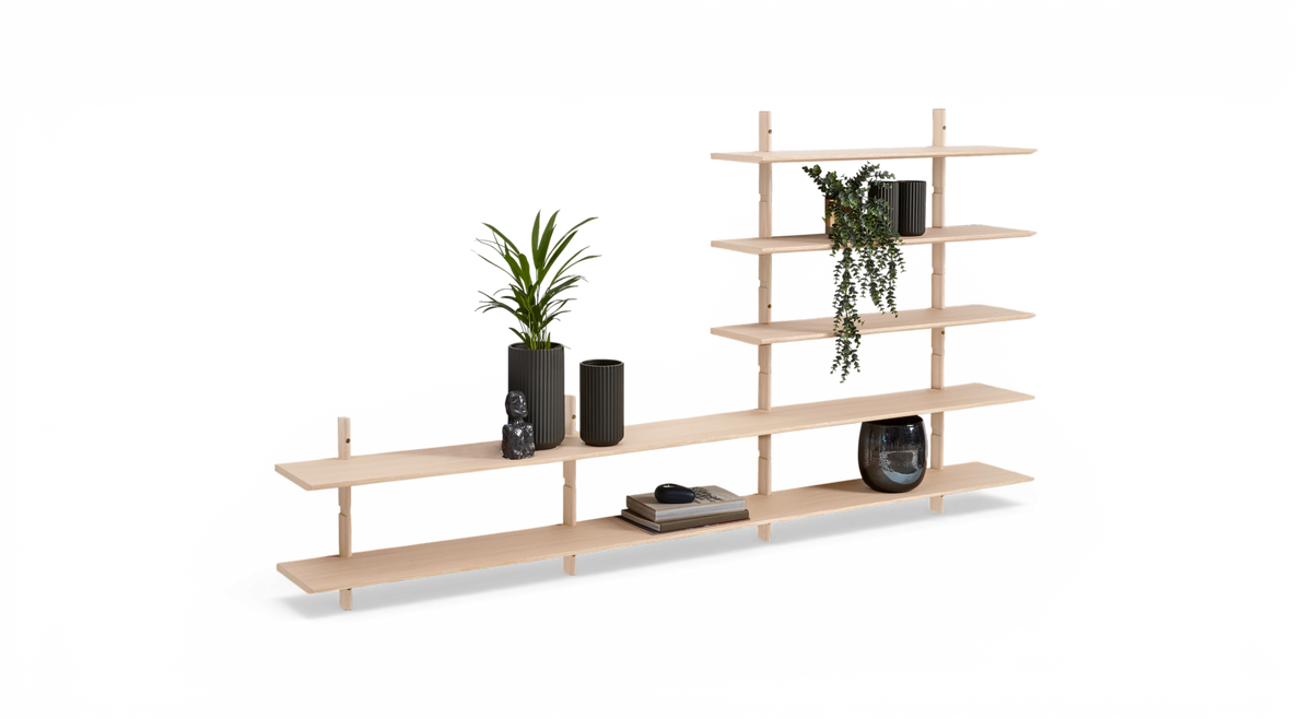 Modulært reolsystem i lyst træ med asymmetriske hylder, stylet med grønne planter, riflede vaser, bøger og en glasvase, frilagt mod hvid baggrund.