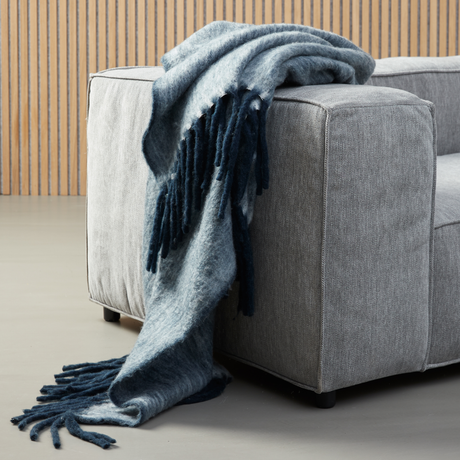 Blå meleret plaid med frynser draperet over armlænet på en grå sofa.