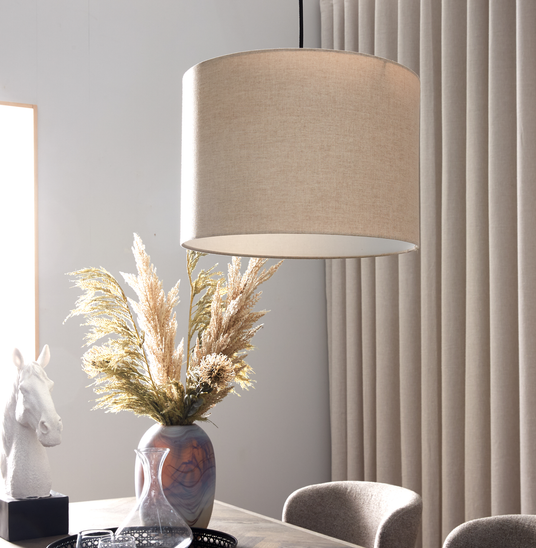 Beige pendellampe over spisebord med vase med pampasgræs og beige gardiner i blødt dagslys.