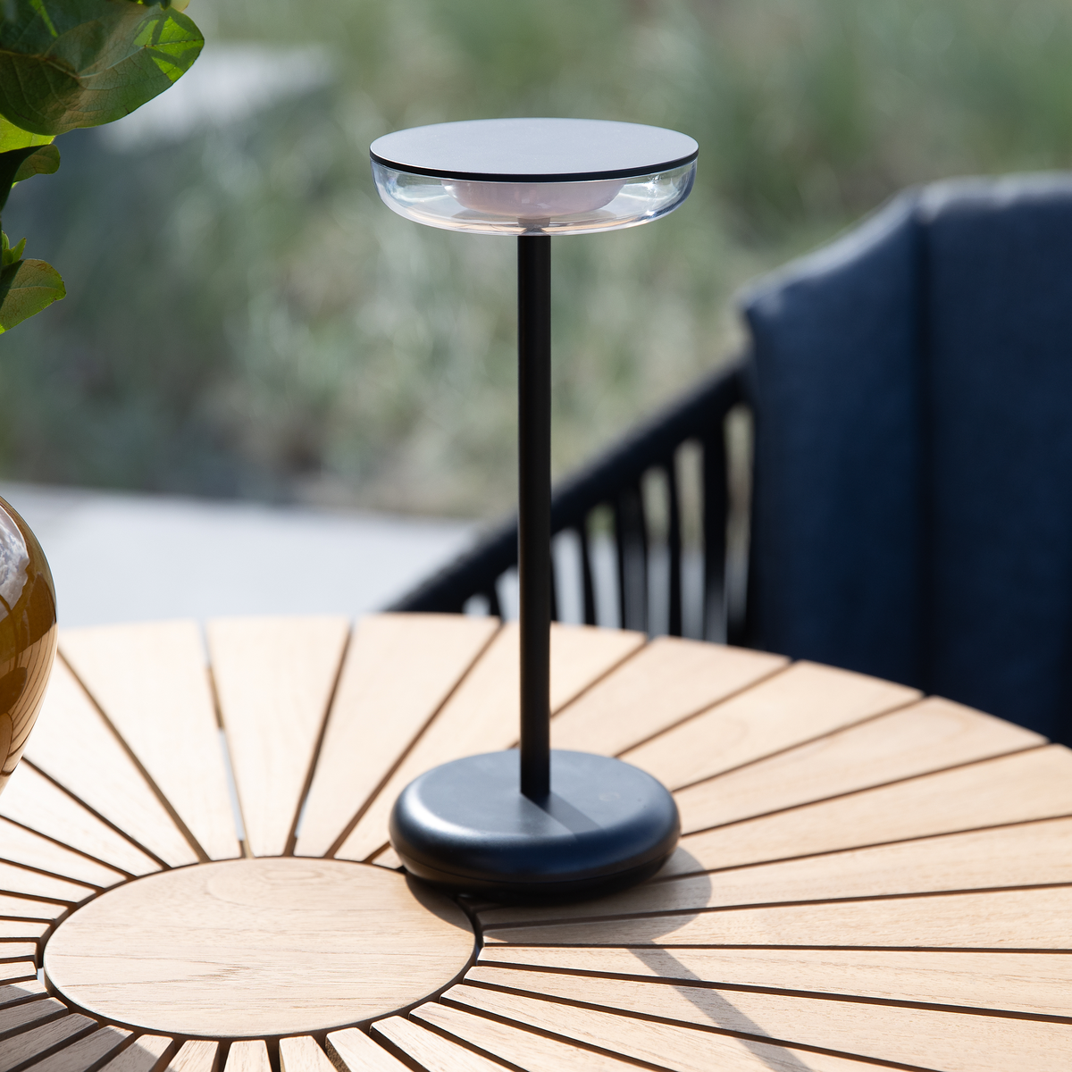 Sort, slank bordlampe på rundt havebord i træ udendørs i dagslys.