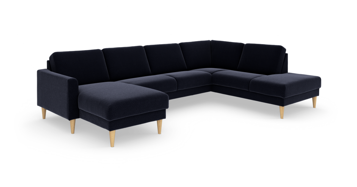 Mørkeblå hjørnesofa/U-sofa med chaiselong i begge ender og koniske ben i lyst træ, frilagt på hvid baggrund.