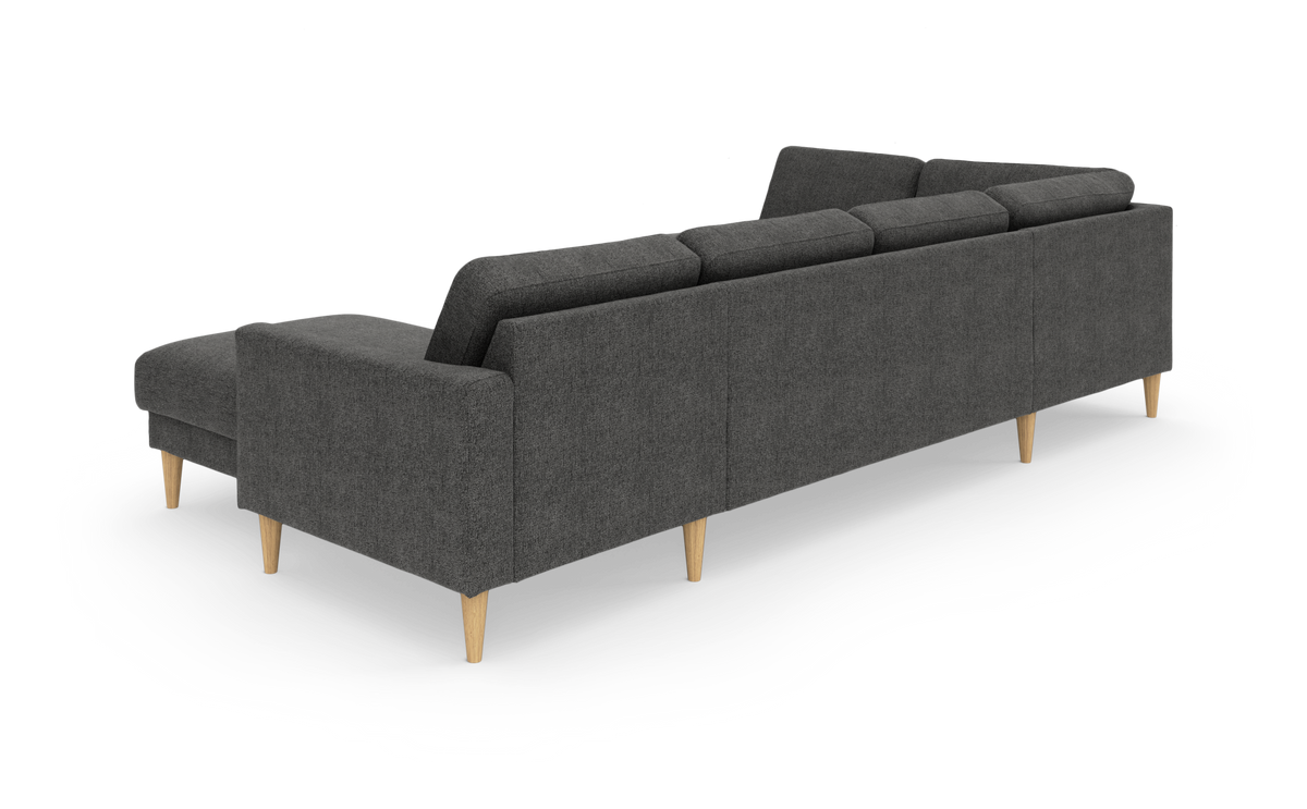 Mørkegrå hjørnesofa med chaiselong, set skråt bagfra, med koniske lyse træben, frilagt på hvid baggrund.