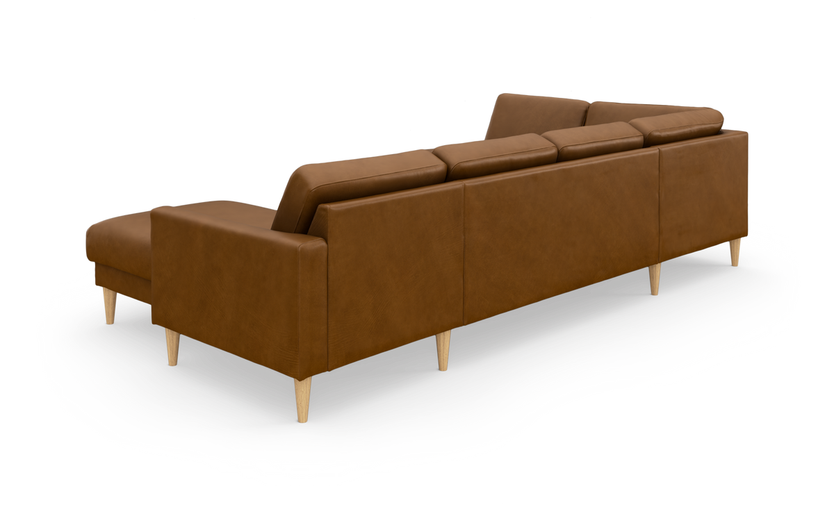 Brun læderhjørnesofa med chaiselong, set bagfra i skrå vinkel, på lyse træben mod frilagt hvid baggrund.
