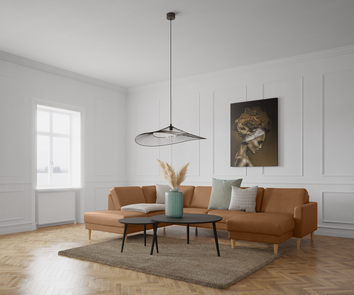 Lys stue med karamelbrun hjørnesofa, sort pendel, to sorte sofaborde, vase med pampasgræs og kunst på væggen.