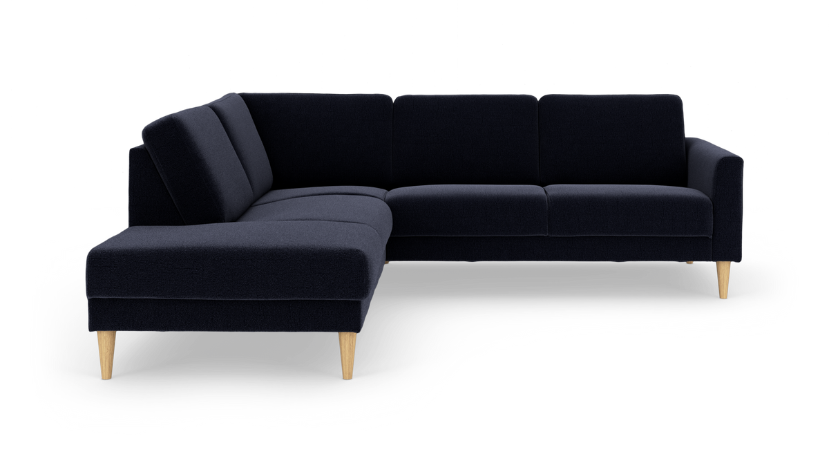 Mørkeblå L‑sofa med chaiselong til venstre og koniske ben i lyst træ.