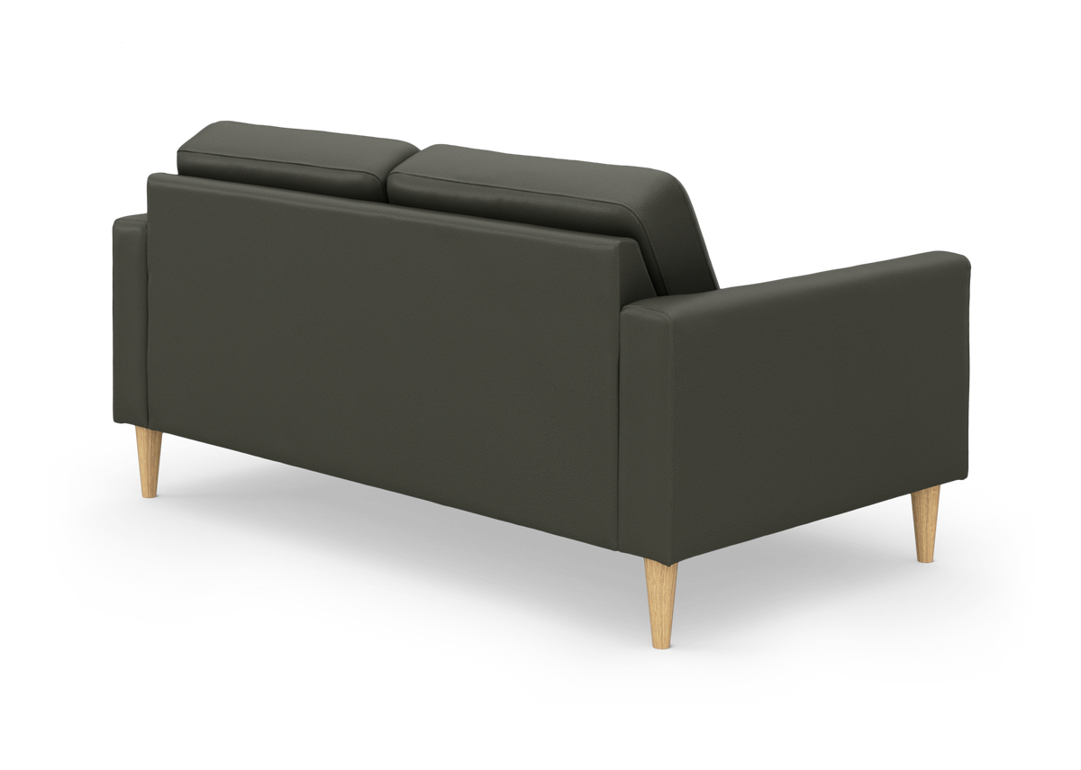 Mørkegrøn sofa med slanke armlæn og lyse, koniske træben set bagfra i vinkel.