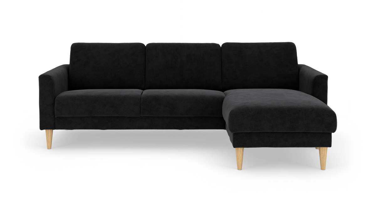 Sort hjørnesofa med chaiselong til højre og lyse træben, frilagt på hvid baggrund.
