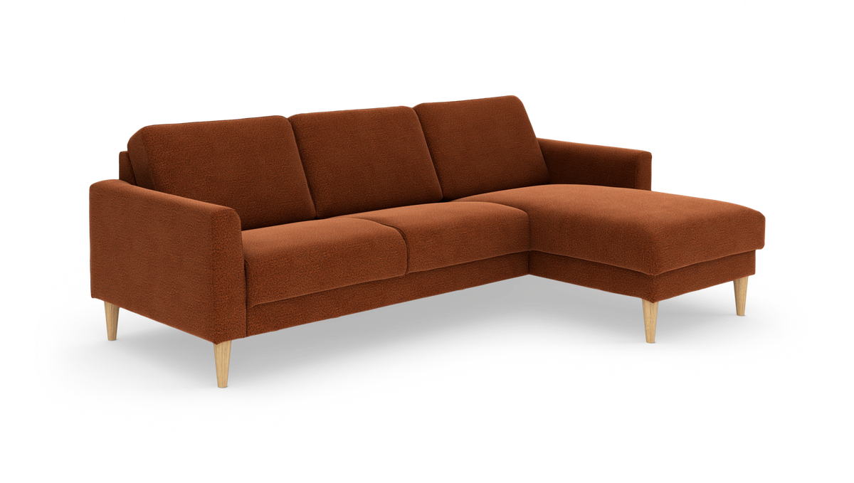 Rustfarvet hjørnesofa med chaiselong til højre og lyse træben, frilagt på hvid baggrund.