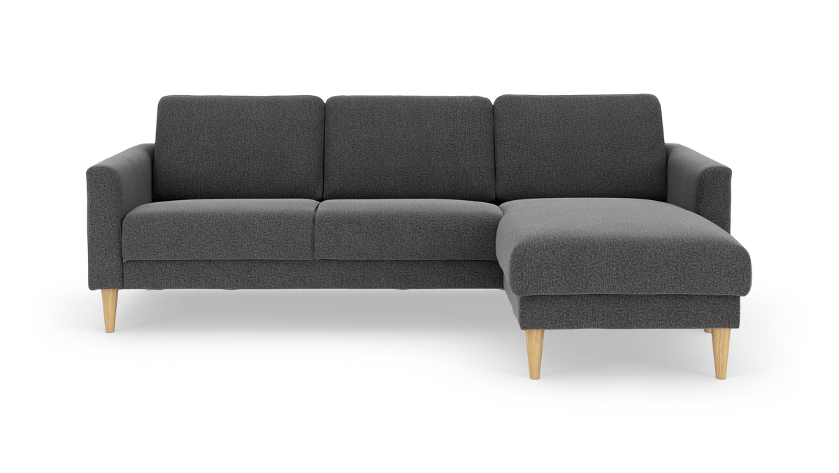 Mørkegrå L-formet 3-personers sofa med chaiselong til højre og lyse træben, frilagt på hvid baggrund.