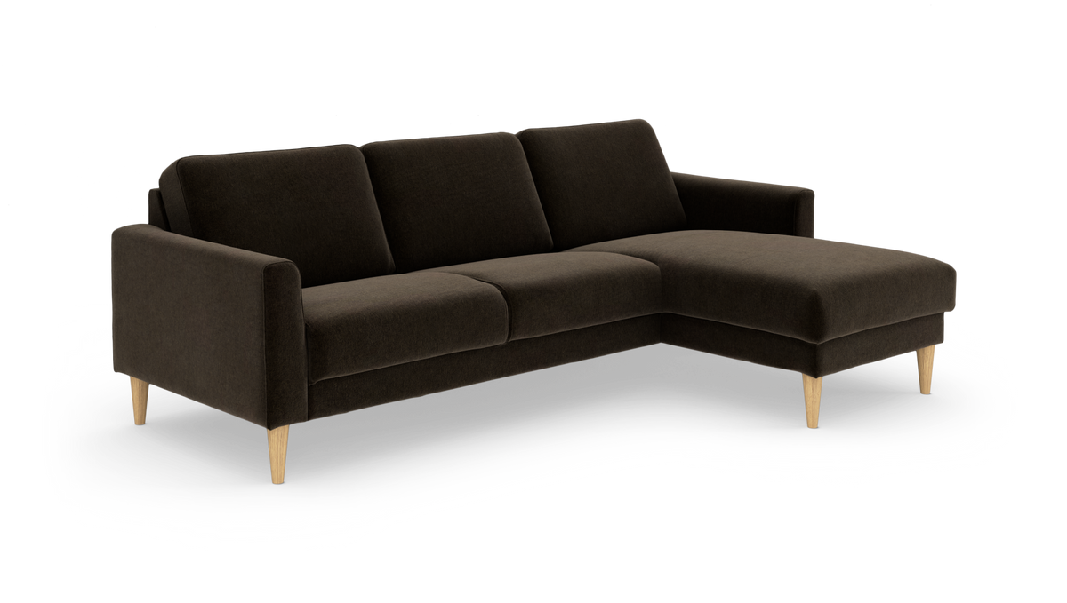 Mørkebrun hjørnesofa med chaiselong til højre og lyse træben, frilagt på hvid baggrund.