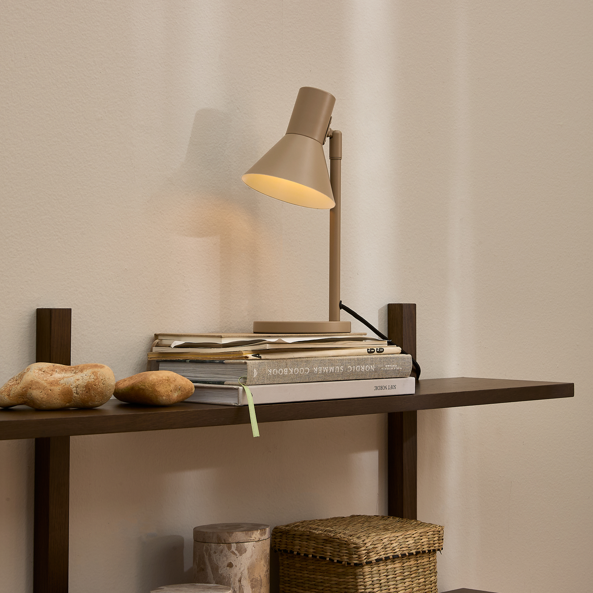 Beige bordlampe på mørk træhylde med bøgerne Nordic Summer Cookbook og Sky Design, natursten og flettet kurv i rolig, minimalistisk indretning.