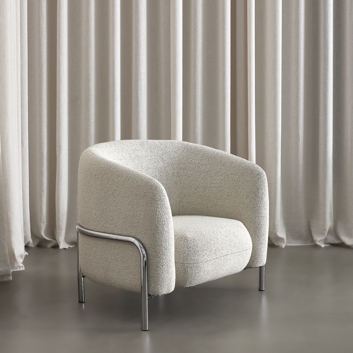 Lys beige bouclé lænestol med afrundede former og kromben foran beige gardiner.