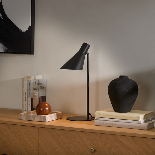 Sort bordlampe på træskænk med sort vase oven på bøgerne Den store bog om maleriets historie, Soft Minimal og A Modern Way to Live; marmorbakke med trækugle og abstrakt vægkunst.