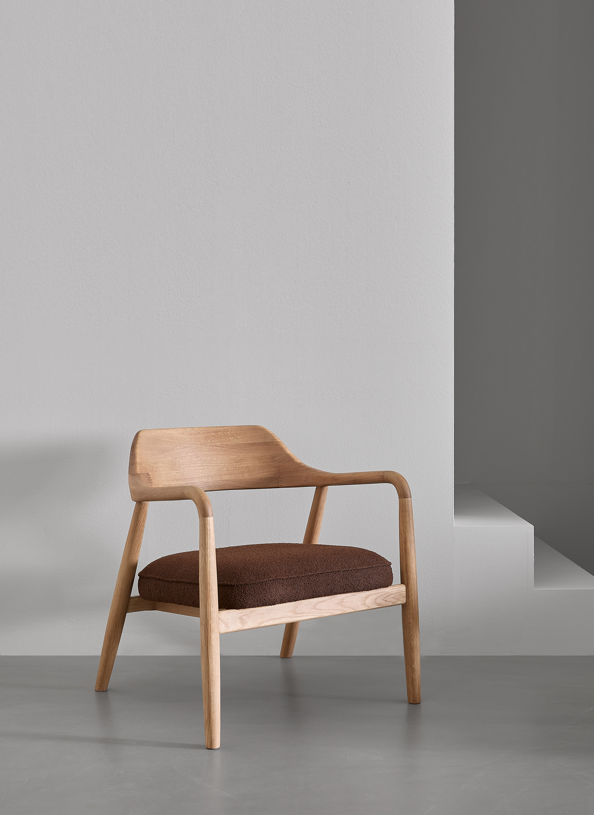 Minimalistisk loungestol i lyst træ med brun hynde i gråt studiomiljø.