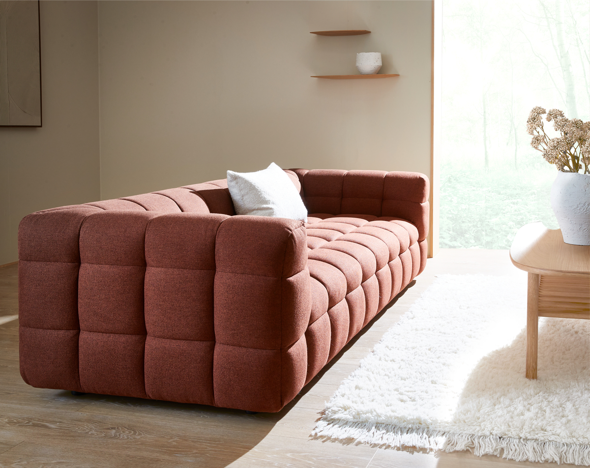Rustfarvet, dybt polstret sofa i stue med hvidt shag-tæppe og træbord i dagslys.