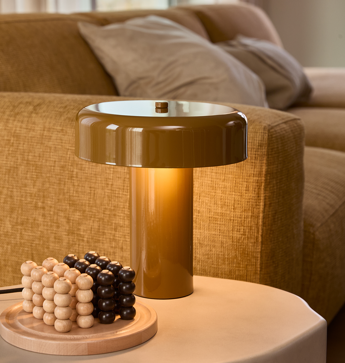 Nærbillede af varm brun bordlampe på et sidebord ved siden af en beige sofa med puder, med trækugler som dekoration på en bakke.