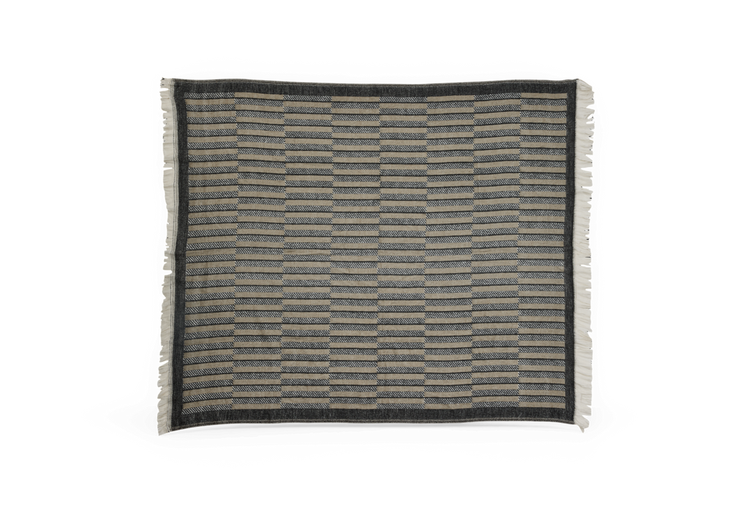 Mønstret, rektangulær plaid i grå og beige med mørk kant og frynser langs siderne.