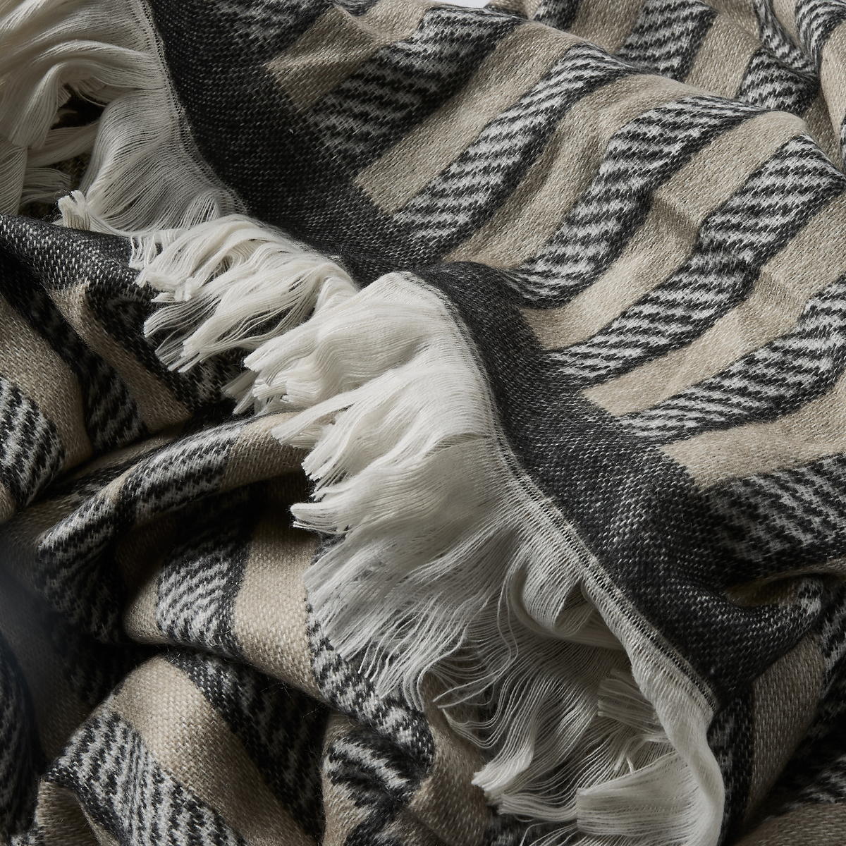 Nærbillede af blød plaid med beige og mørkegråt zigzagmønster og hvide frynser.