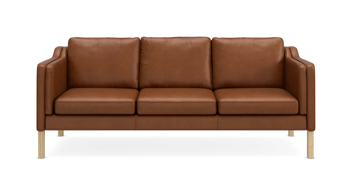 Brun lædersofa med tre sædehynder og lyse træben, frilagt på sort baggrund.