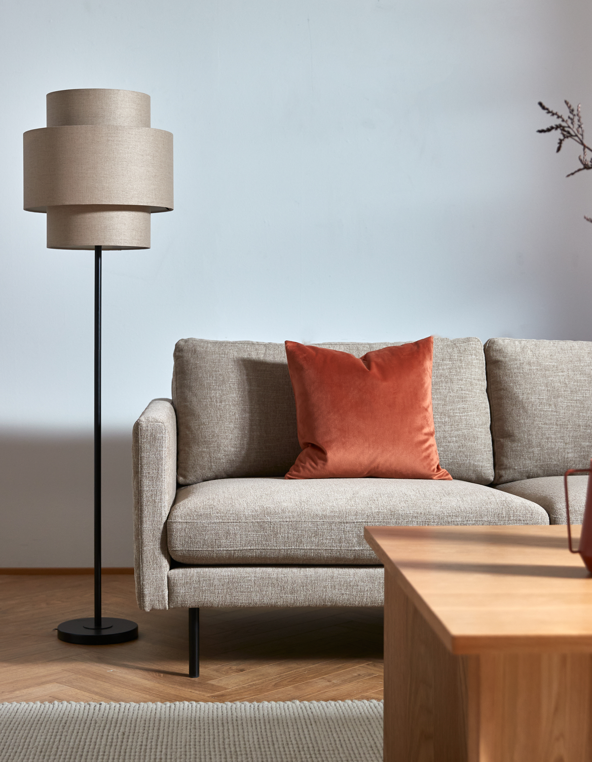 Beige sofa med rustfarvet pude ved siden af en gulvlampe og træ-sofabord i en lys, minimalistisk stue.