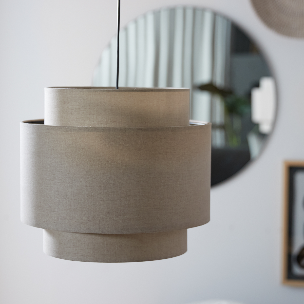 Beige stofpendel i lagdelt, moderne design i en lys stue med rundt spejl i baggrunden.