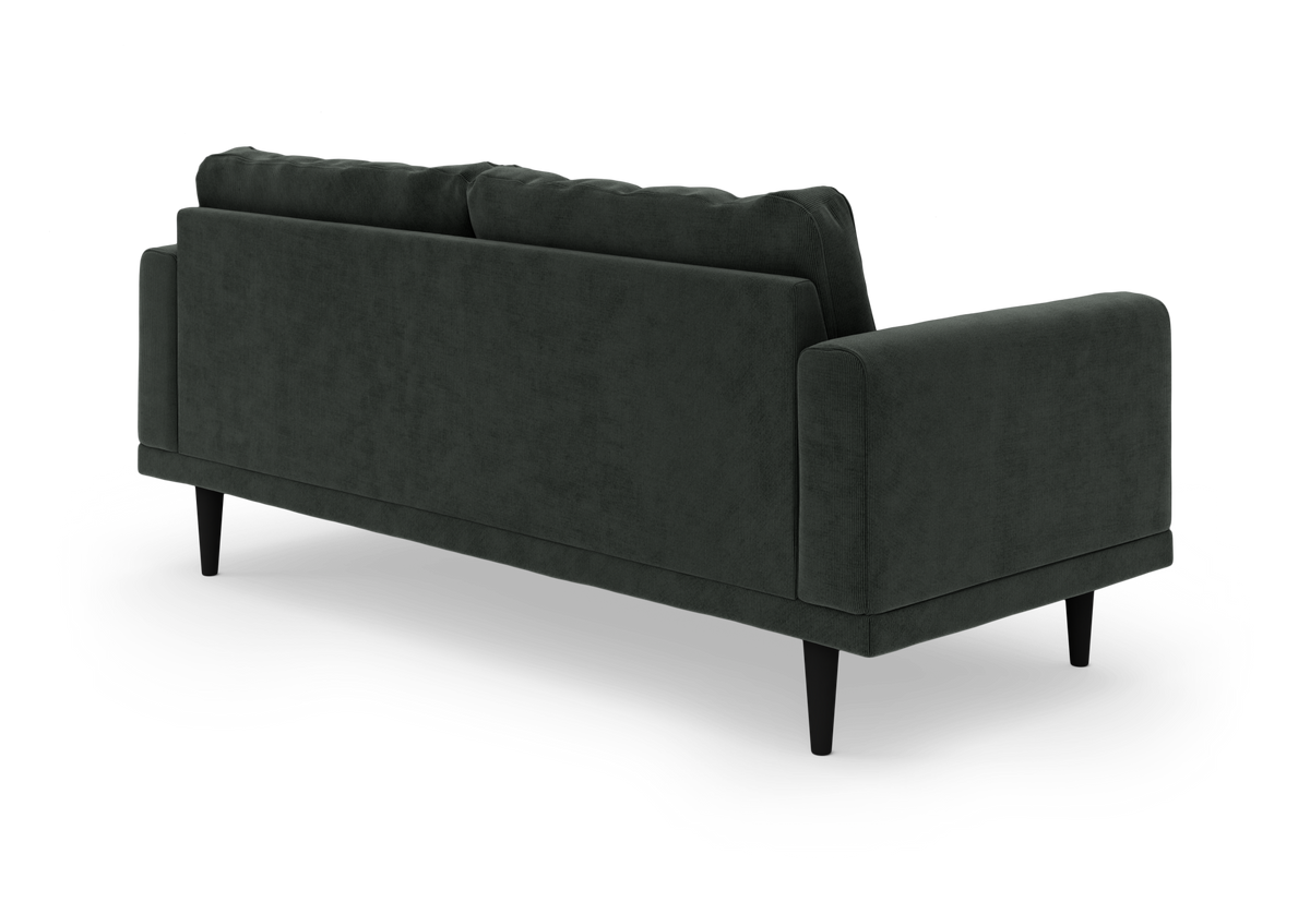 Mørkegrøn 3-personers sofa i velour med slanke sorte ben, vist bagfra i skrå vinkel.