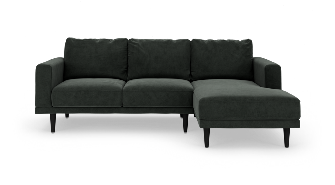 Mørkegrøn hjørnesofa med chaiselong til højre, på slanke sorte ben, fritlagt mod hvid baggrund.