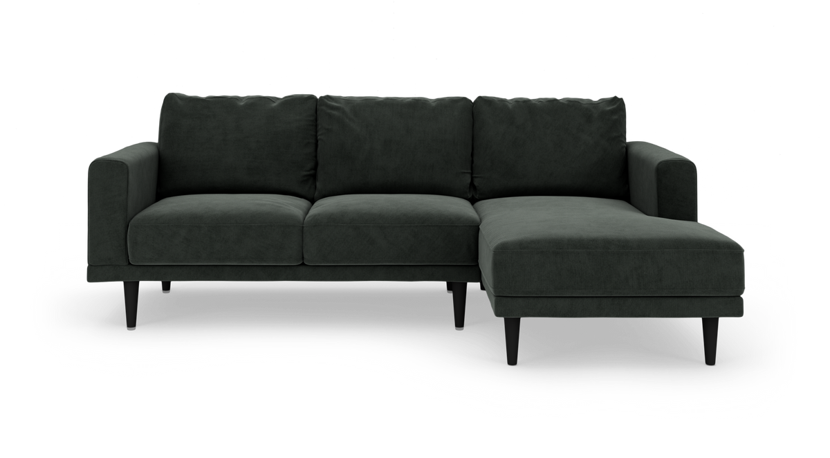 Mørkegrøn hjørnesofa med chaiselong til højre, på slanke sorte ben, fritlagt mod hvid baggrund.